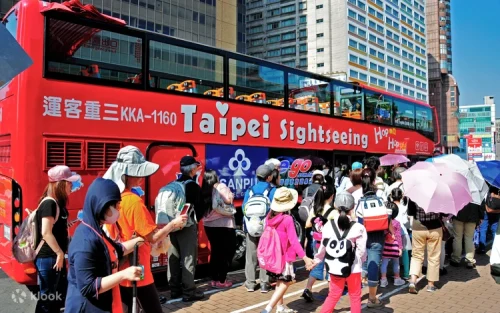 Red open-top sightseeing bus passing by the iconic Taipei 101