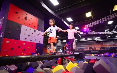 Climber scaling the indoor rock wall above a safe foam landing pad