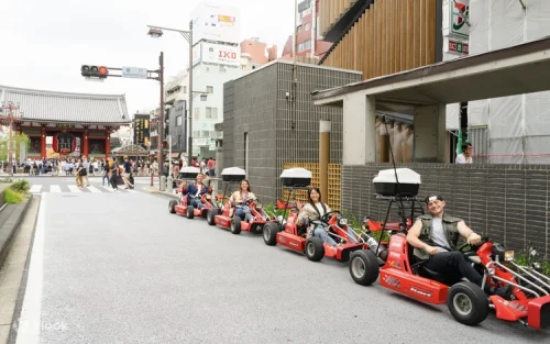 Bystanders taking photos of go-kart drivers cruising through the vibrant streets of Japan