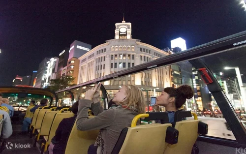Red open-top sightseeing bus driving past the iconic Tokyo Tower